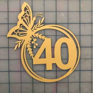 May include: Gold-colored paper cutout of a butterfly with floral accents surrounding the number 40. The number is in a circle.