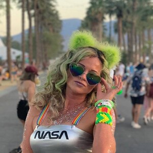 May include: A woman wearing a silver crop top with the word "NASA" printed on it, green glitter on her body, and a green bikini bottom. She is wearing sunglasses and green furry cat ears.