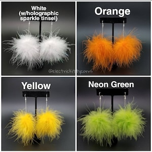 May include: Four pairs of feather earrings in different colors: white with holographic sparkle tinsel, orange, yellow, and neon green. The earrings are displayed on a black stand with silver chains.