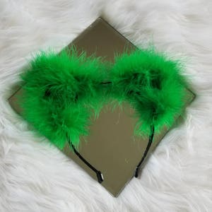 May include: Green feather headband with a black elastic band. The headband is made of fluffy feathers and is perfect for adding a touch of whimsy to any outfit.