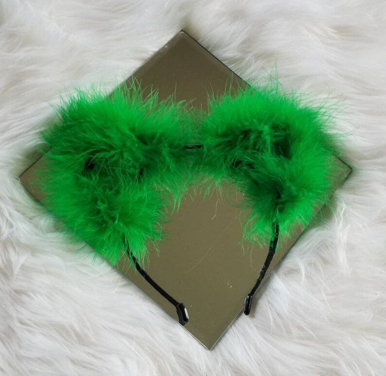 May include: Green feather headband with a black elastic band. The headband is made of fluffy feathers and is perfect for adding a touch of whimsy to any outfit.
