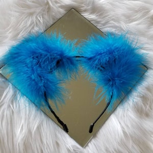 May include: A headband with two large, fluffy blue feather ear pieces. The headband is black and the feathers are a bright, vibrant blue.