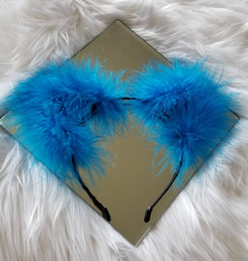 May include: A headband with two large, fluffy blue feather ear pieces. The headband is black and the feathers are a bright, vibrant blue.
