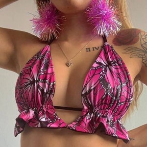 May include: Pink halter top with a butterfly print and ruffled trim. The top has a plunging neckline and a black strap across the chest.