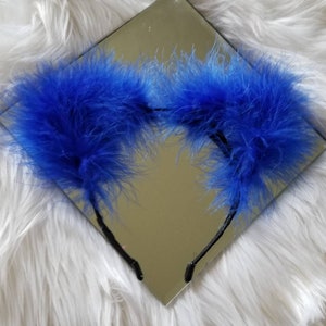 May include: A pair of blue feather headband earmuffs. The earmuffs are made of soft, fluffy feathers and are attached to a black headband.
