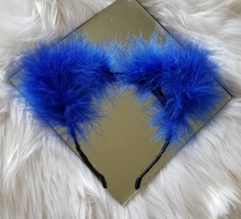 May include: A pair of blue feather headband earmuffs. The earmuffs are made of soft, fluffy feathers and are attached to a black headband.