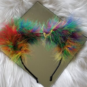 May include: A rainbow colored fluffy headband with two large pom-poms on either side.