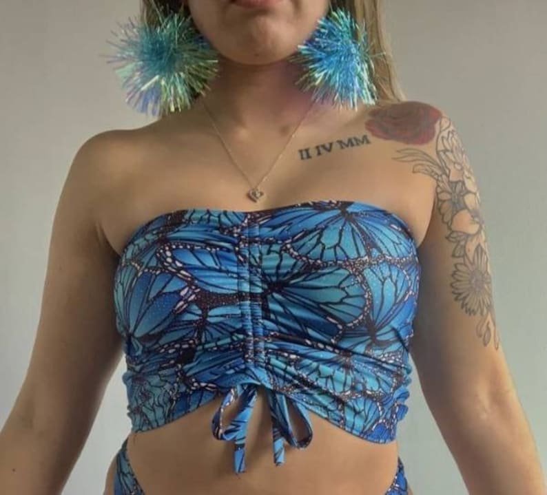 May include: A blue strapless top with a butterfly print. The top has a gathered detail at the bust and ties at the front.