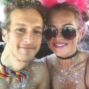 May include: A couple covered in glitter, wearing festive accessories. The woman has pink hair and is wearing a pink furry headband with cat ears. The man is wearing a rainbow bow tie.