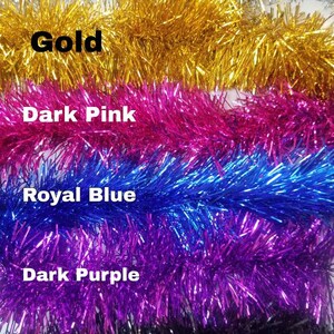 May include: A close-up of six spools of metallic tinsel garland. The spools are arranged vertically, with the colors silver, gold, dark pink, royal blue, dark purple, and black. The text "@electrickittycorns" is visible at the bottom of the image.