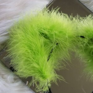 May include: A close-up of a bright green feather boa. The boa is soft and fluffy, and it is perfect for adding a touch of fun and whimsy to any outfit.