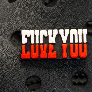 May include: A black and white charm with the text "Frick You Love You" in red and white letters.