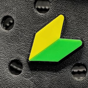 May include: A close-up of a black textured surface with a yellow and green Japanese car emblem.