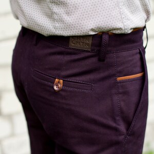 May include: A pair of dark purple pants with a brown leather patch on the back pocket. The patch has the text "CHYN CHYN" on it.