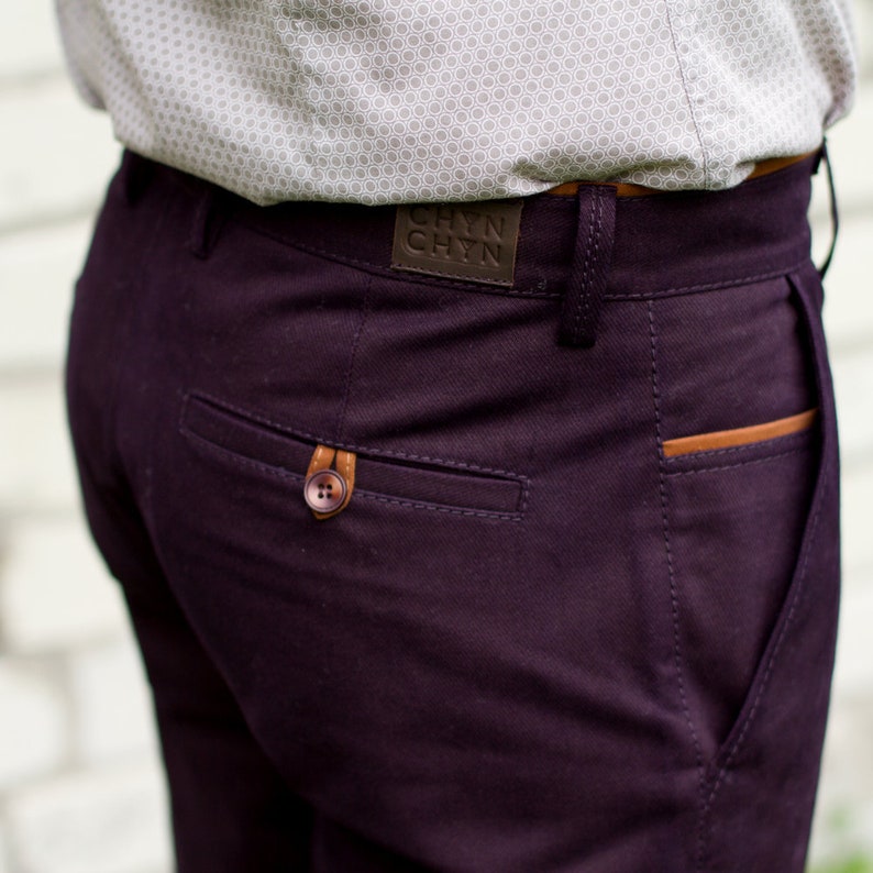 May include: A pair of dark purple pants with a brown leather patch on the back pocket. The patch has the text "CHYN CHYN" on it.