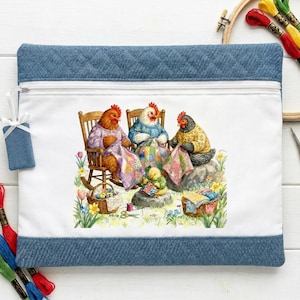 May include: A rectangular zippered pouch with a white center panel featuring a colorful illustration of three chickens and a chick quilting in a garden. The pouch has blue quilted fabric borders at the top and bottom and a small blue fabric zipper pull.