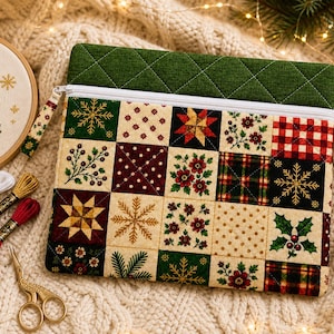 May include: A rectangular quilted zipper pouch featuring a patchwork design of various holiday-themed fabric squares, including snowflakes, holly, plaid, and floral patterns, topped with a solid green quilted border and a white zipper closure.