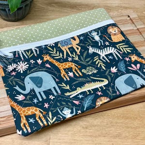 May include: A quilted fabric pouch with a zip closure. The pouch features a dark teal background with a repeating pattern of safari animals, including giraffes, elephants, and zebras. The top edge is a light green with white polka dots.