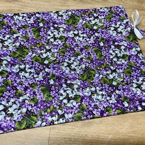 Puede incluir: Una tela de estampado floral morado y blanco con un dise&ntilde;o acolchado. La tela tiene una cinta blanca unida a una esquina.
