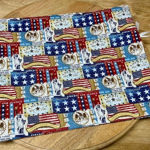 Pu&ograve; includere: Un sottopentola trapuntato rettangolare con un design patriottico. Il tessuto presenta motivi ripetuti della bandiera americana, stelle e testo patriottico in rosso, bianco e blu. Un anello bianco &egrave; attaccato per appenderlo.