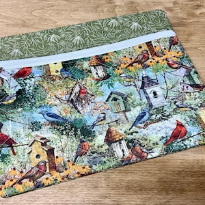 May include: A green zippered pouch with a birdhouse and bird print. The pouch has a white zipper and a green and white floral print on the back.