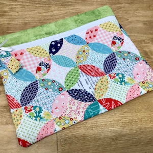 May include: A colorful zippered pouch with a patchwork design featuring various shades of pink, red, blue, green, and yellow. The pouch is made of fabric and has a green zipper.