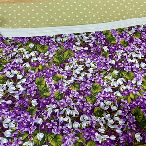 Puede incluir: Una bolsa con cremallera de estampado floral morado y blanco con un forro de tela verde con lunares. La bolsa est&aacute; hecha de tela acolchada.