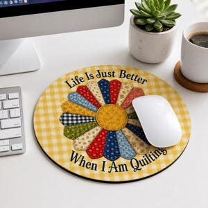 May include: A round mouse pad with a yellow and white gingham background featuring a central flower design made of multi-colored patterned fabric petals. The text reads Life Is Just Better When I Am Quilting in dark blue lettering.
