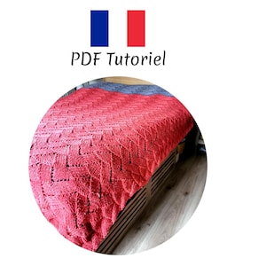 May include: A close-up of a red knitted blanket with a diamond pattern. The blanket is folded and draped over a bed.