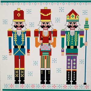 May include: Three pixel art nutcracker figures. The nutcracker on the left is wearing a blue and red suit with a yellow hat. The nutcracker in the middle is wearing a red and green suit with a yellow hat. The nutcracker on the right is wearing a green and purple suit with a gold crown.