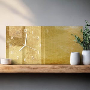May include: A rectangular wall clock with a gold-colored face and white numerals. The clock hands are white. The clock is displayed on a wooden shelf with decorative items, including small white vases and a small white bowl.