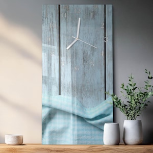 May include: A rectangular wall clock with a light blue wooden background and silver hands and numerals. The clock has a light blue and white checkered fabric at the bottom. The clock is displayed on a wooden surface.
