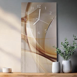 May include: A rectangular wall clock with a beige and brown abstract design. The clock face features white numerals and hands. The clock is displayed on a wooden surface with decorative items and plants.