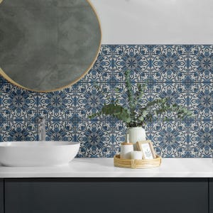 May include: A bathroom vanity with a white ceramic sink and a round mirror with a wooden frame. The backsplash is a blue and white patterned tile with a floral design. There are decorative items on the counter, including a vase with greenery, a small bottle, and a picture frame.