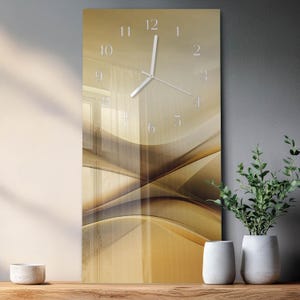 May include: A rectangular wall clock with a gold and brown abstract design. The clock face has white numerals and hands. The clock is displayed on a wooden surface with decorative vases and greenery.