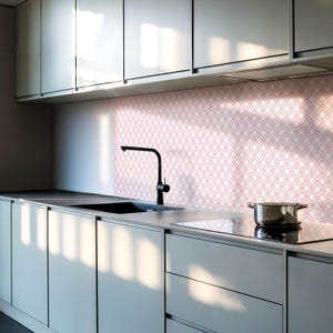 Puede incluir: Una cocina moderna con armarios grises y un salpicadero de patrón rosa. Un grifo negro está montado sobre un fregadero de acero inoxidable. Una placa de cocción eléctrica negra es visible en primer plano.