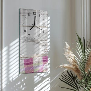 May include: A rectangular wall clock with a white, distressed wood-look face. Black numerals mark the hours. The bottom section features a pink and purple plaid pattern. The clock hands are black.