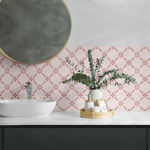 May include: A bathroom vanity with a pink and red patterned tile backsplash. A round mirror hangs above a white porcelain sink. A vase with green foliage sits on the counter, along with a small tray holding two bottles of soap.