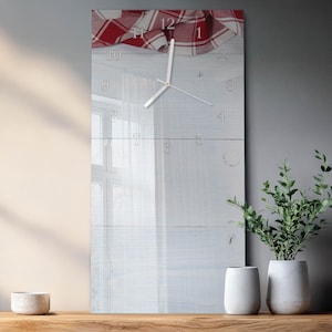 May include: A rectangular wall clock with a white face and silver hands. The clock face has a light wood grain appearance with etched numerals. A red and white checkered cloth drapes over the top. The clock is displayed on a wooden surface.