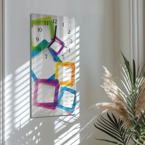 May include: A rectangular wall clock with a white background and colorful geometric shapes. The clock face features black numerals and hands. The shapes are in shades of green, blue, purple, orange, and yellow.