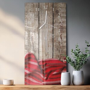 Könnte beinhalten: Eine rechteckige Wanduhr mit Holzplanken-Design. Das Zifferblatt hat silberne Zeiger und Ziffern. Eine rot-weiß gestreifte Decke ist unten drapiert. Die Uhr wird auf einem Holzregal mit weißen Vasen und Grünpflanzen ausgestellt.