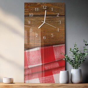 May include: Rectangular wall clock with a wooden background and white numerals. The clock hands are white, and the bottom half of the clock features a red and white checkered pattern. The clock is displayed on a wooden surface.