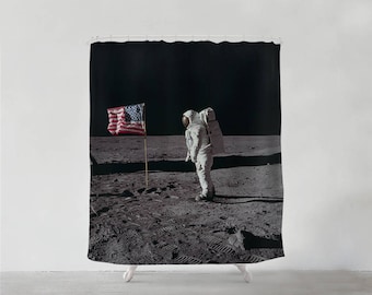 Könnte beinhalten: Ein Schwarzweißfoto eines Astronauten, der die amerikanische Flagge auf dem Mond pflanzt. Der Astronaut trägt einen weißen Raumanzug und steht auf einer grauen, felsigen Oberfläche. Die amerikanische Flagge weht im Wind.