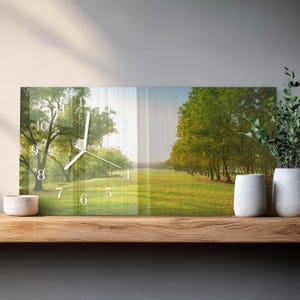 May include: A rectangular wall clock featuring a scenic landscape of a park with trees and a grassy field. The clock face has white numerals and hands. The clock is displayed on a wooden shelf with white vases and greenery.