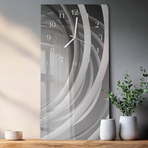 May include: A rectangular wall clock featuring a black and white abstract design of overlapping curved lines. The clock face displays white Arabic numerals from 1 to 12 arranged in a circle, with two thin white hands indicating the current time.