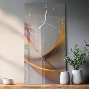 May include: A rectangular wall clock with a modern design. The clock face features a gradient of colors, with a blend of orange, yellow, and brown hues. The clock hands and numerals are silver. The clock is displayed on a wooden surface.