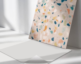 May include: A sheet of white adhesive paper with a corner peeled back, revealing a patterned adhesive sheet underneath. The patterned sheet features a terrazzo design with blue, green, yellow, and orange chips on a beige background.