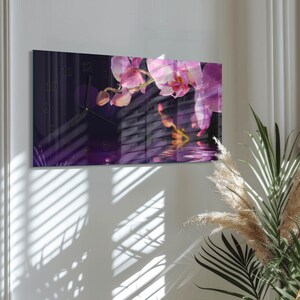 May include: Rectangular wall clock featuring a floral design with pink orchids. The clock face has black numerals and hands, set against a dark purple background. The image includes a reflection effect, enhancing the floral theme.