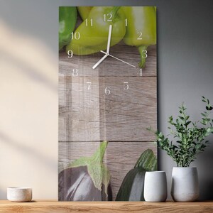 May include: A rectangular wall clock featuring a wooden background with green bell peppers and eggplants. The clock face has white numbers and hands. The clock is a decorative kitchen or dining room accent.