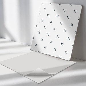 May include: A white sheet of paper with a repeating pattern of small black crosses. The paper is lying on a white surface with a shadow.